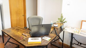 A wooden desk with a laptop, a chair, a small plant, and a sign on the wall. - Siesta Motel (Colfax)
