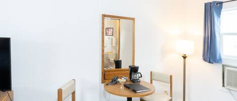 Habitación de hotel con una mesa redonda, dos sillas, cafetera, lámpara y un espejo grande.