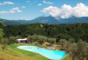A swimming pool with a mountain backdrop, surrounded by trees and a small building.