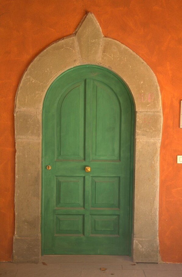 A green door with a stone archway, set against an orange wall.