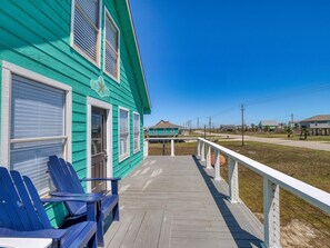 A green building with a covered porch, blue Adirondack chairs, and a white railing.