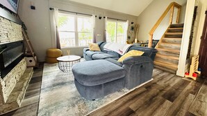A living room with a sofa, ottoman, and a small round table. There is a staircase to the right and a window with curtains. - Casa Mia by the Braves Stadium In Smyrna Ga (Smyrna)