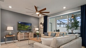 A modern living room with a beige leather sofa, a wooden coffee table, a TV mounted on the wall, and a ceiling fan. - Themed Pool Home w/ Resort Amenities Near Disney (Davenport)