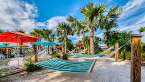 A beach area with hammocks, umbrellas, and palm trees. - Themed Pool Home w/ Resort Amenities Near Disney (Davenport)