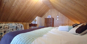 A bedroom with a sloped ceiling, a bed with patterned bedding, a dresser, and a lamp. - Chalet (Saint Jean Port Joli)