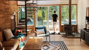 Un interior moderno con techo de madera, una escalera, un ventanal grande, un sofá, una mesa de centro y una chimenea.