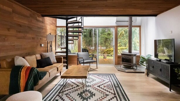 Una sala de estar moderna con techo de madera, escalera espiral, ventana grande, sofá, mesa de centro, televisor y chimenea.