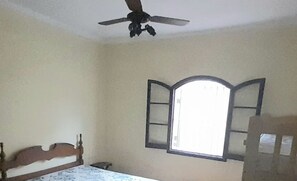 A bedroom with a bed, a ceiling fan, a window, and a chair.