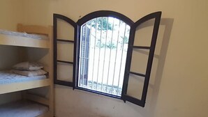 Een kamer met een stapelbed, een raam met een metalen traliewerk en uitzicht op groen buiten.