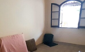 A room with a single window, a pink blanket on a chair, and a dark cushion on the floor.