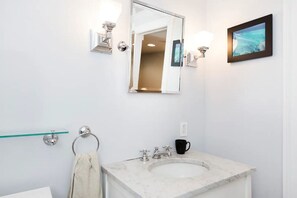 A bathroom with a marble sink, a towel rack, a framed picture on the wall, and a glass shelf. - Private Garden Room in Victorian Home! (San Francisco)