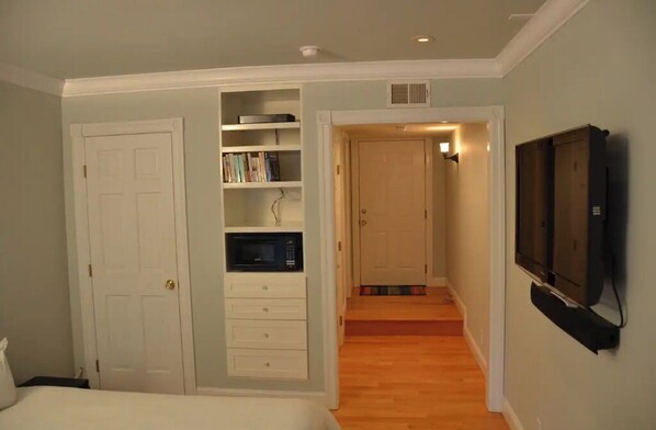 A bedroom with a built-in bookshelf, a microwave, a TV mounted on the wall, and a door leading to a hallway.