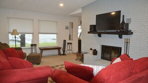 A living room with red sofas, a fireplace, a mounted TV, and a view of the outdoors. - Make memories in this cozy water front house on Eagle Mountain Lake. (Azle)