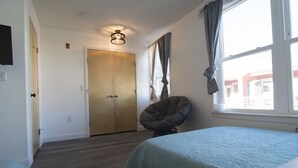 Un dormitorio con dos camas, un ventanal con cortinas, una lámpara en el techo y una puerta que da a otra habitación.