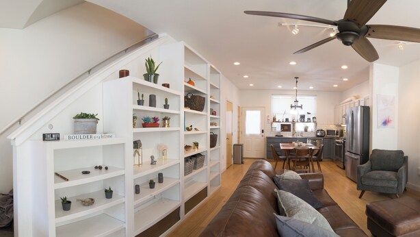 Una sala de estar moderna con un sofá de cuero marrón, una zona de comedor con mesa y sillas, una cocina con armarios y electrodomésticos blancos, y un televisor de pantalla plana grande.