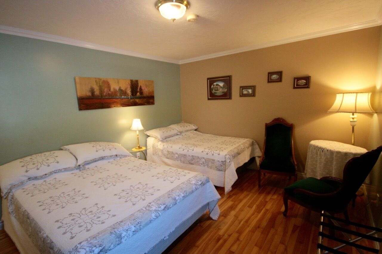 Una habitació amb dos llits, una cadira, un taulell i un quadre penjat a la paret.