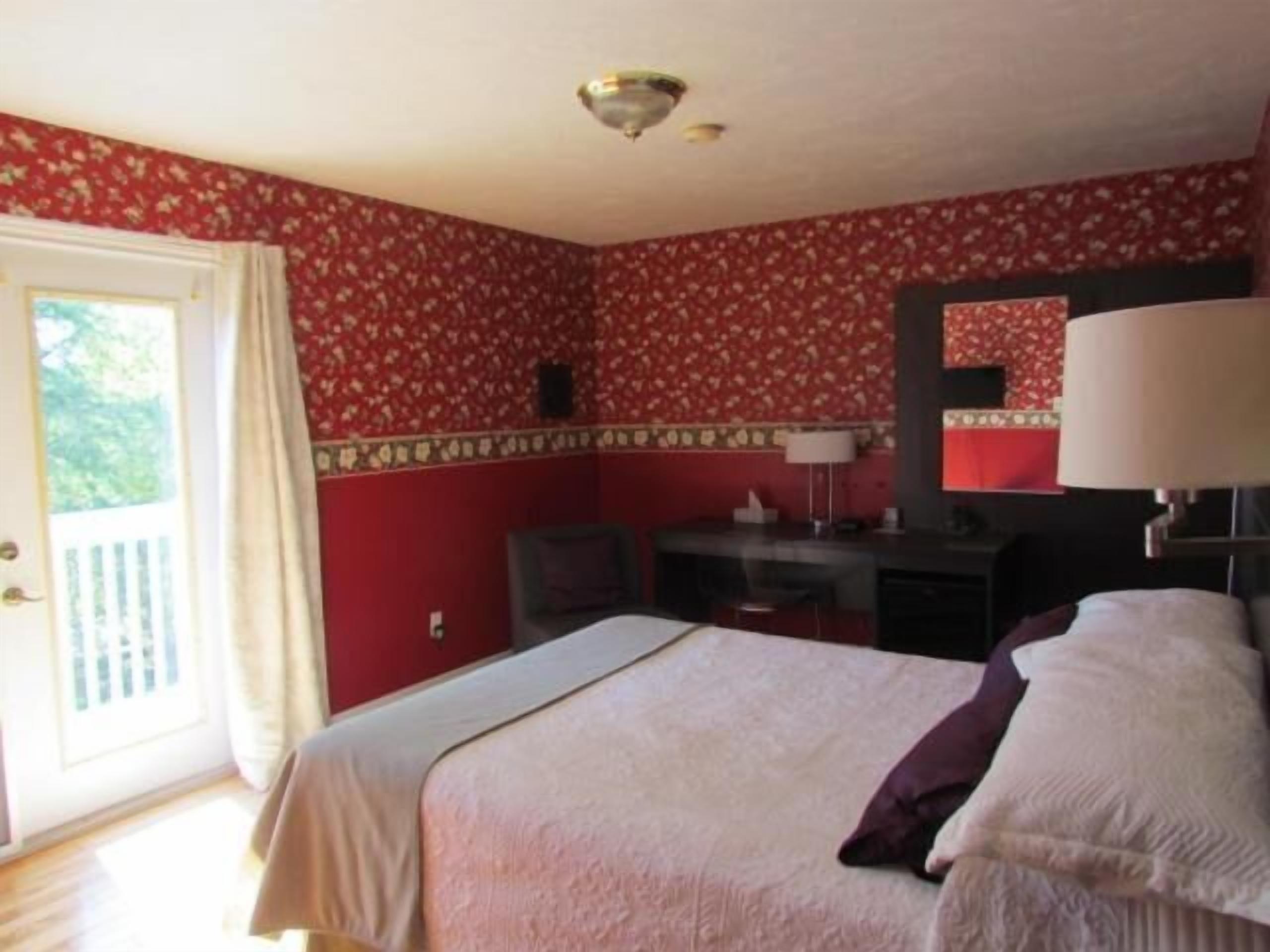 Een kamer met een bed, een bureau, een stoel, een spiegel en een deur die uitkomt op een balkon.