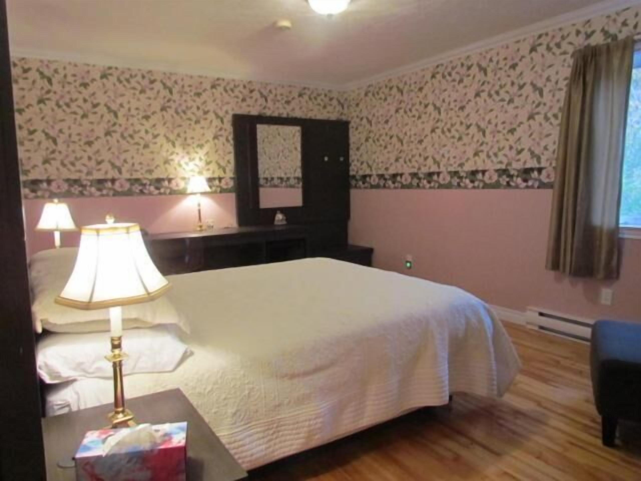 Une chambre d’hôtel avec un lit, deux lampes de chevet, une commode, un miroir et une fenêtre avec des rideaux.