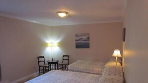 A hotel room with two beds, a small table with chairs, and two wall-mounted lamps. - Shepody Bay Inn (Shepody)