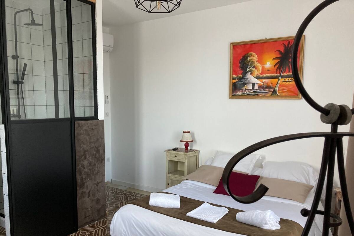 A hotel room with a bed, a nightstand, a lamp, and a painting of a sunset.