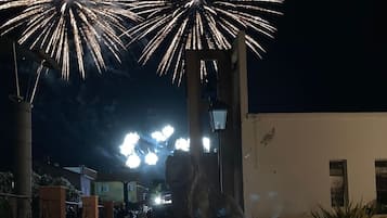 A nighttime scene with fireworks display, a pathway, and a building with a light fixture.