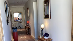 Um corredor com carpete estampado, quadros enquadrados e uma mesa com objetos decorativos.