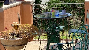Uma área de pátio ao ar livre com uma mesa redonda e cadeiras, cercada por plantas e flores em vasos.