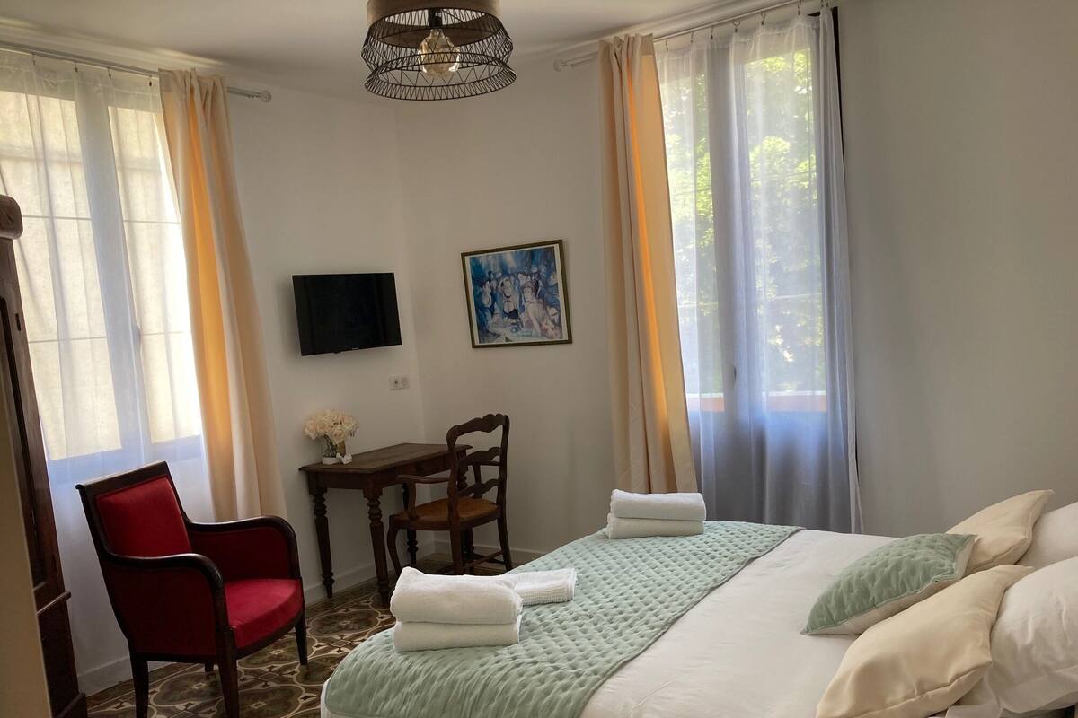 A hotel room with a bed, a desk, a chair, a television, and a painting on the wall.