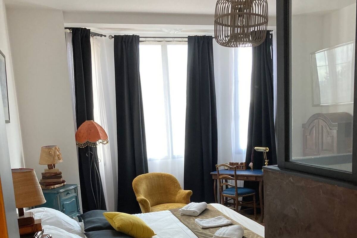 A hotel room with a bed, two chairs, a desk, a lamp, and a patterned floor.