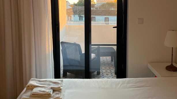 Hotellihuone, jossa on sänky, ikkuna, josta on näkymä rakennuksiin, tuoli ja lamppuvarustettu pöytä.