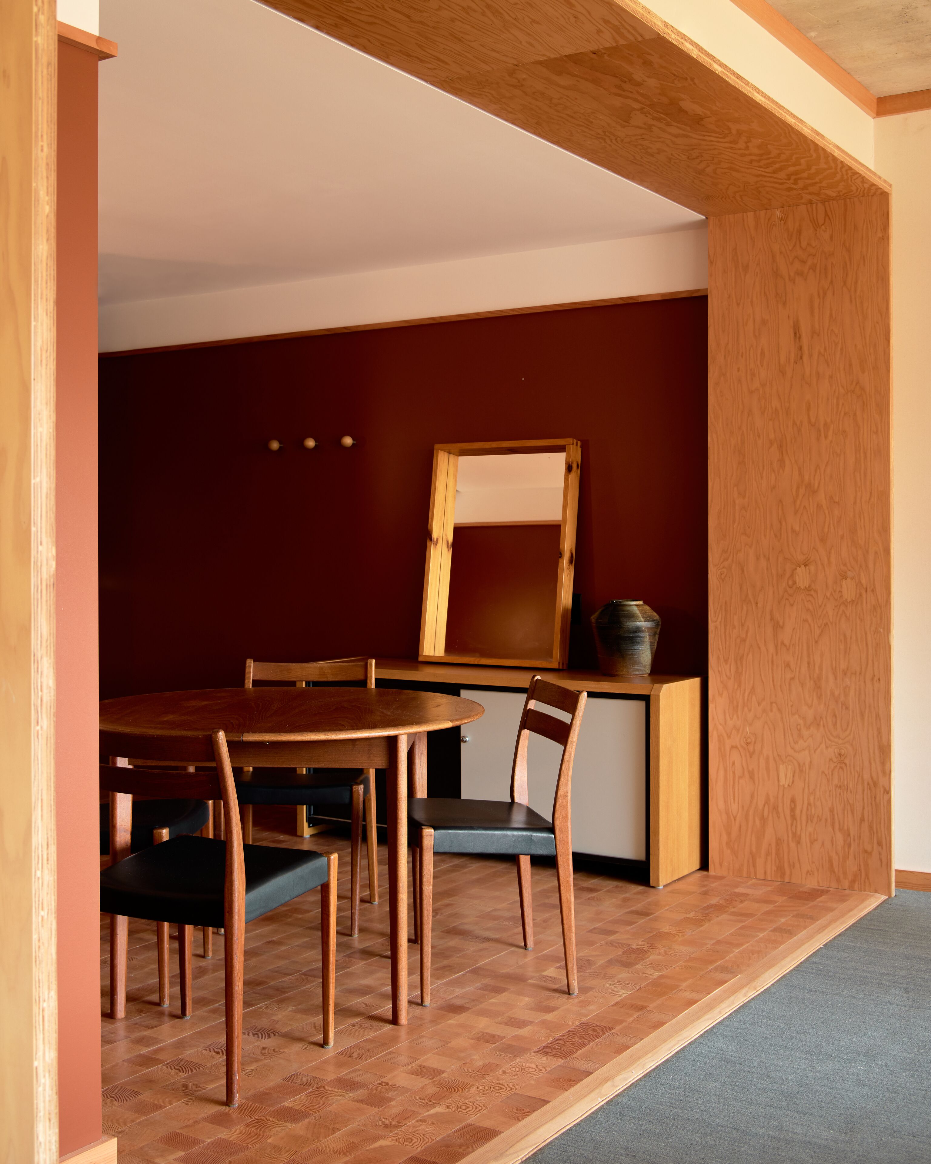 A dining area with a wooden table and chairs, a mirror, and a small cabinet.