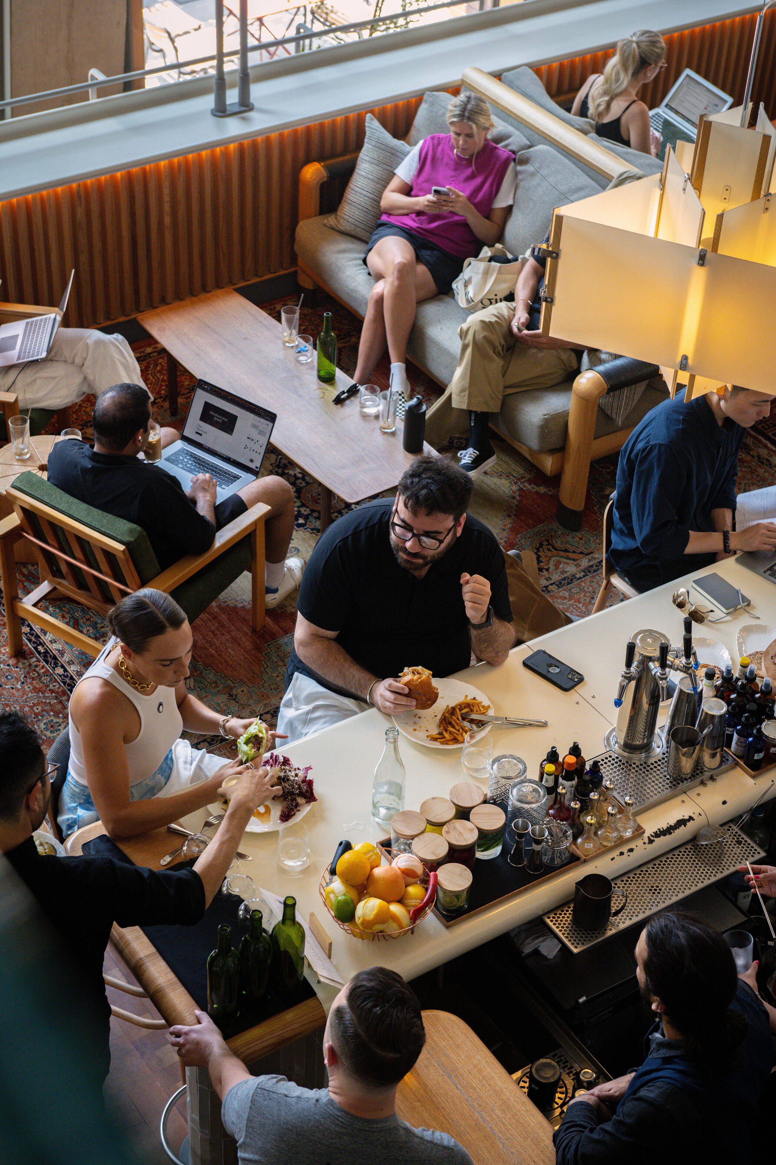 A group of people dining in a modern, well-lit room with a bar area, comfortable seating, and a view through large windows.