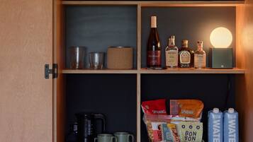 Een houten kast met planken, gevuld met diverse voorwerpen zoals flessen, bekers en een koffiezetapparaat.