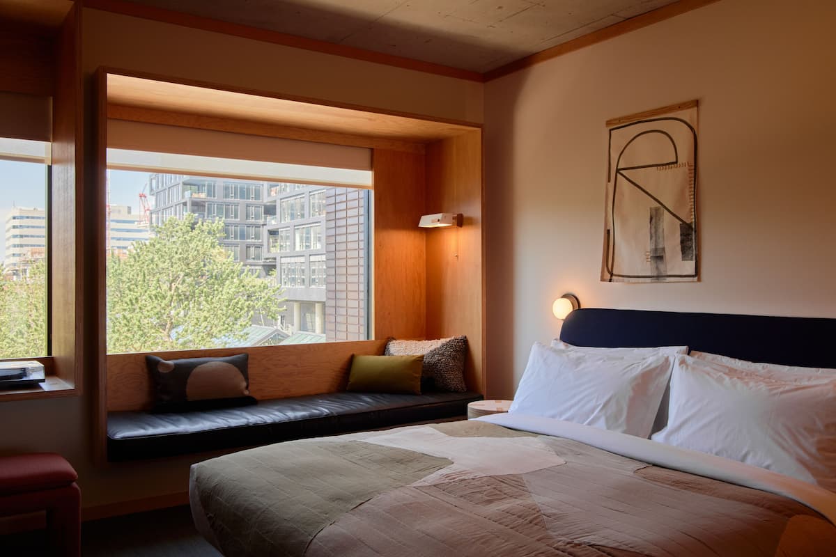 Una habitación de hotel moderna con una cama grande, un banco empotrado junto a la ventana y vistas de la ciudad.