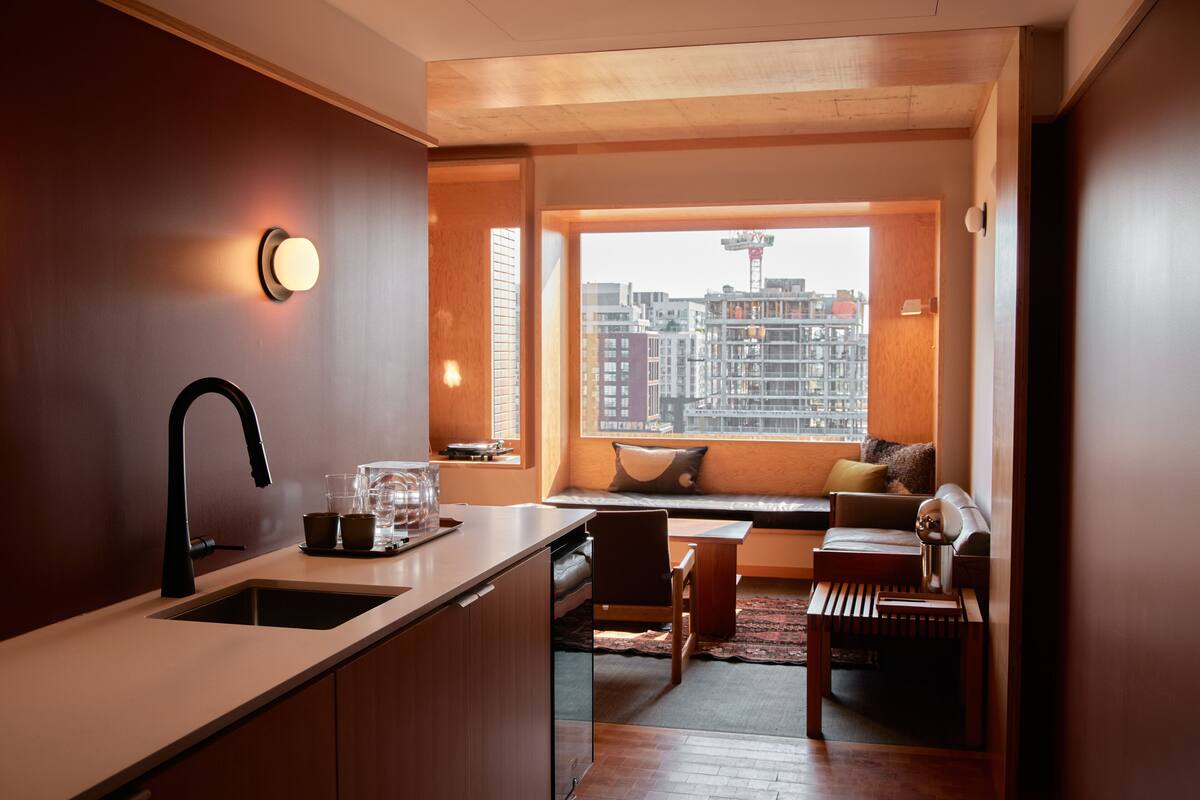 Una cocina moderna con un lavamanos, una zona de comedor con un banco y vistas a un paisaje urbano a través de un ventanal grande.