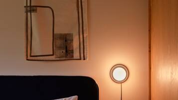 A neatly made bed with white linens, a round table lamp, and a wall-mounted abstract artwork.