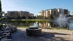 Un patio frente al lago con sillones de descanso, una fogata y una fuente.