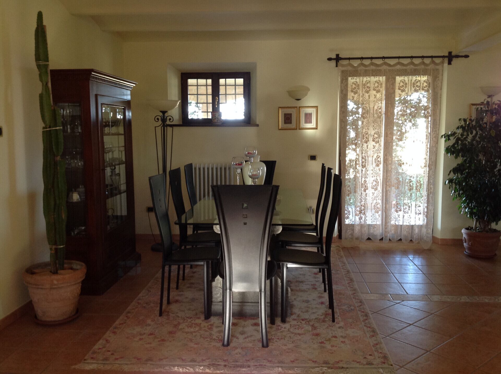 A dining area with a table and chairs, a radiator, a window with curtains, and a potted plant.