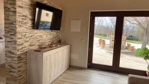A modern kitchen with a stone backsplash, a flat-screen TV mounted above the counter, and a sliding glass door leading to an outdoor area. - Villa Giulia - Homelike Villas (Appignano)