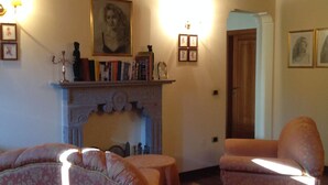 A cozy living room with a fireplace, floral-patterned furniture, and wooden beams on the ceiling. - Villa Giulia - Homelike Villas (Appignano)