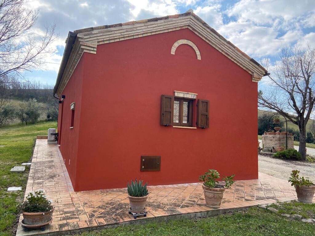 Ein rotes Gebäude mit einem kleinen Fenster und einer Tür, umgeben von Blumentöpfen und einem gepflasterten Weg.