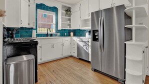 A modern kitchen with white cabinets, a stainless steel refrigerator, and a wooden floor. - Walk to Main St  • Hot Tub • Backyard Oasis (Fredericksburg)