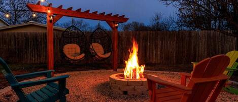 Patio trasero con un hogar, dos mecedoras y una pérgola de madera.