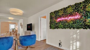 A modern living room with a neon sign, a flat-screen TV, and blue sofas. - Walk to Main St • Hot Tub • Backyard Oasis (Fredericksburg)