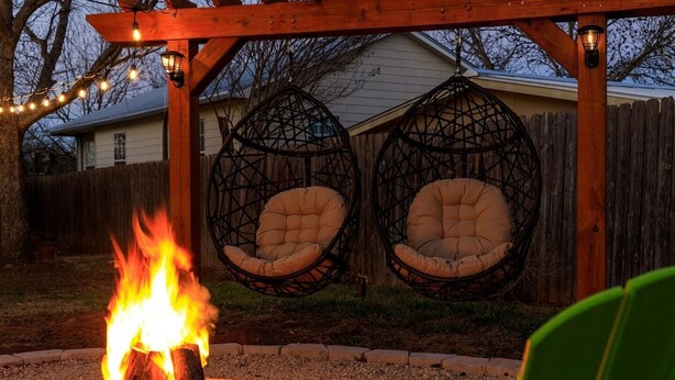 A backyard with a fire pit, two hanging chairs, and a wooden pergola with string lights. - Walk to Main St • Hot Tub • Backyard Oasis (Fredericksburg)