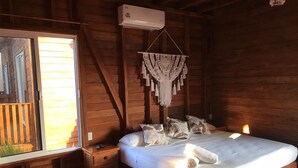 Una habitación de madera con cama, mesita de noche, un colgante de macramé y una ventana.