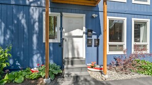 A blue building with a white door, numbered mailboxes, and a small garden with plants and flowers. - The Alpenglow Loft - 1 Bed/1Bath- Radiant Charmer (Anchorage)