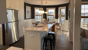 A modern kitchen with a stainless steel refrigerator, white cabinetry, and a central island with stools. - Vitamin Sea-Beautiful Oceanfront-3 Bedroom Condo Located in Duck, NC. (Duck)
