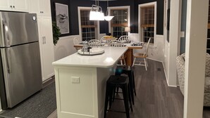 A compact kitchen with white cabinets, a stainless steel refrigerator, a central island with stools, and a pendant light. - Vitamin Sea-Beautiful Oceanfront-3 Bedroom Condo Located in Duck, NC. (Duck)