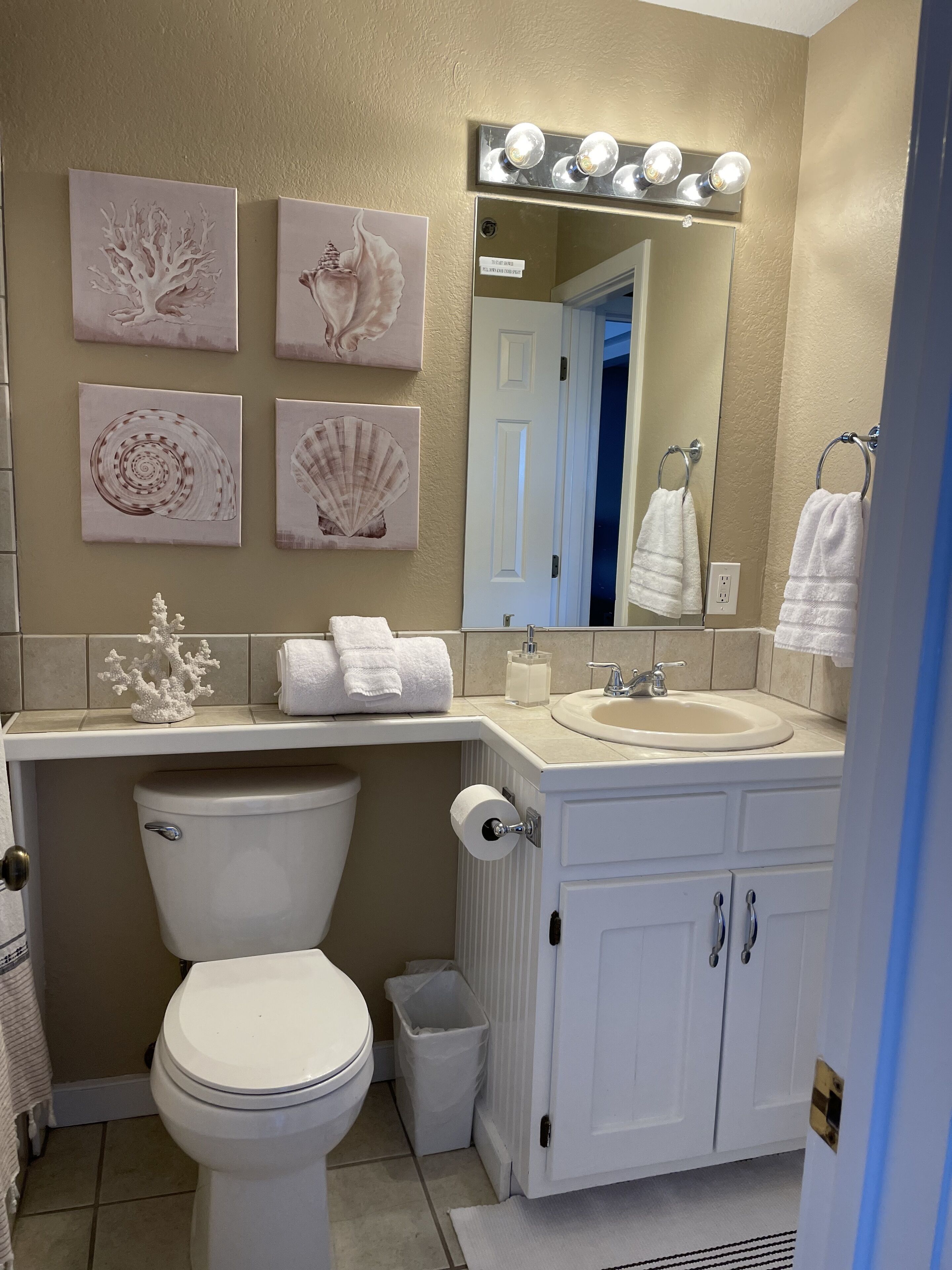 A bathroom with a toilet, sink, and mirror. There are towels and a trash can.